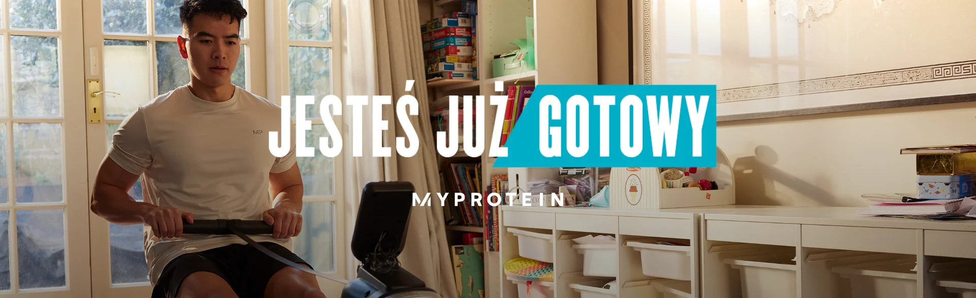 A man workout out on a rowing machine at home with the words 'You're Already Ready - MYPROTEIN' overlaying.